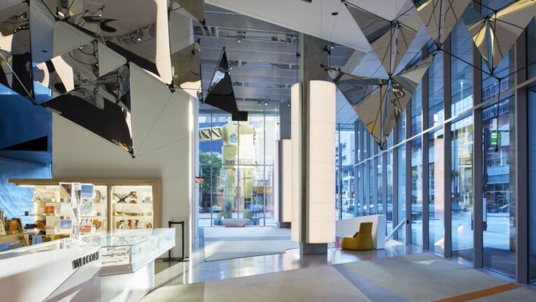 Picture of lobby of Contemporary Art center with large glass windows, concrete columns, and mirrored art hanging from the ceiling.