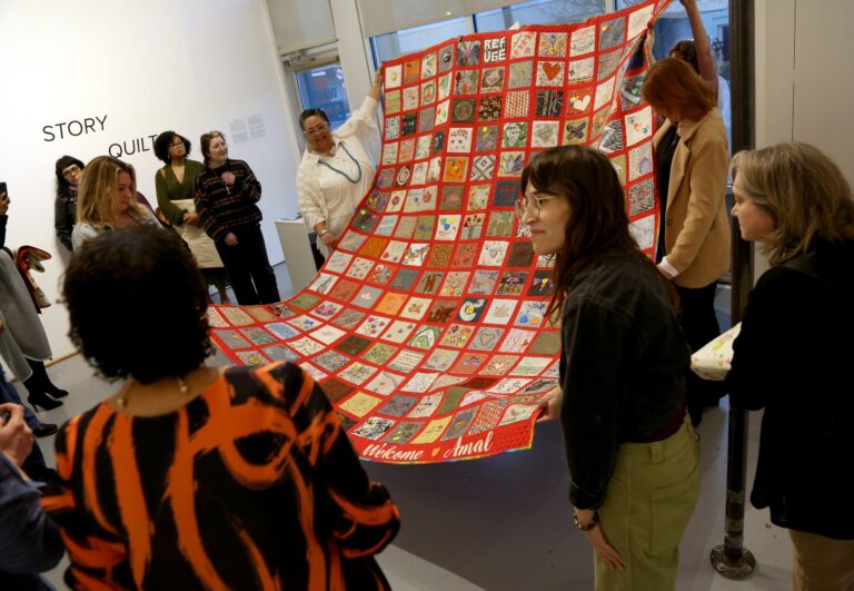 Group of people surrounding a multi-colored quilt made as part of the Truth and Reconciliation Project.