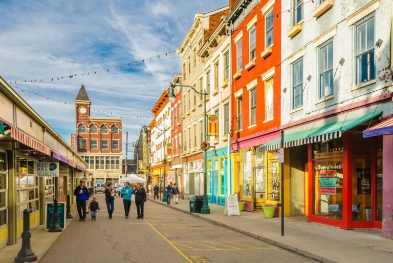 Shoppers walking down a pedestrian street in Findlay Market, a historic commerce area in Cincinnati. Colorful buildings line the walkway.